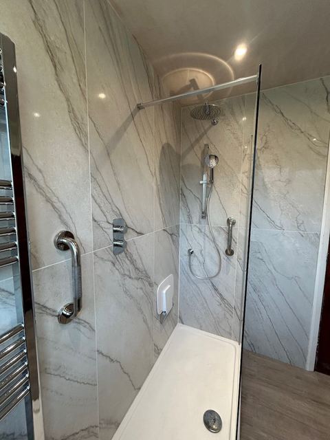 A bath-to-shower conversion with a low-level tray, grab rail and marble-effect tiling